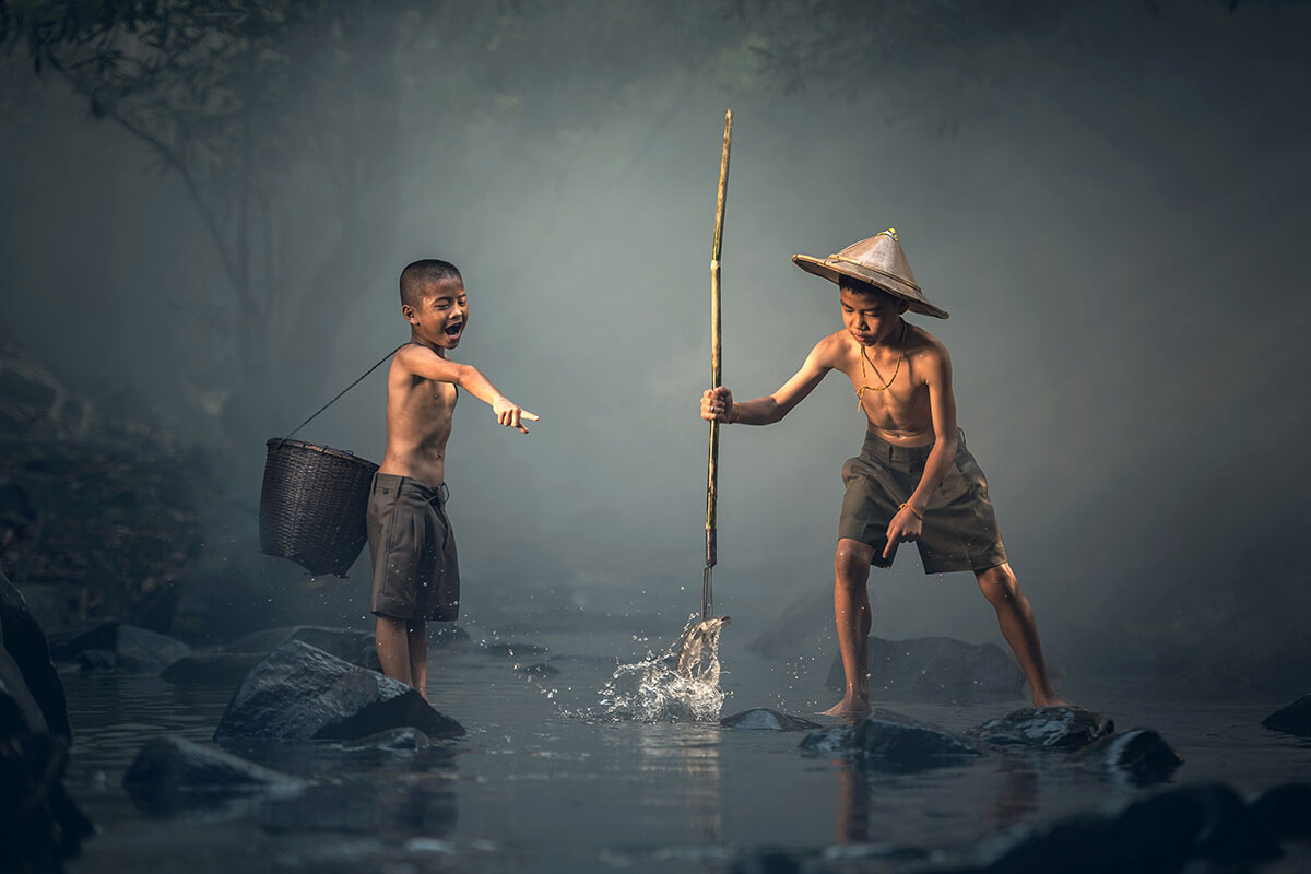 two boys standing in a river with a stick and a basket